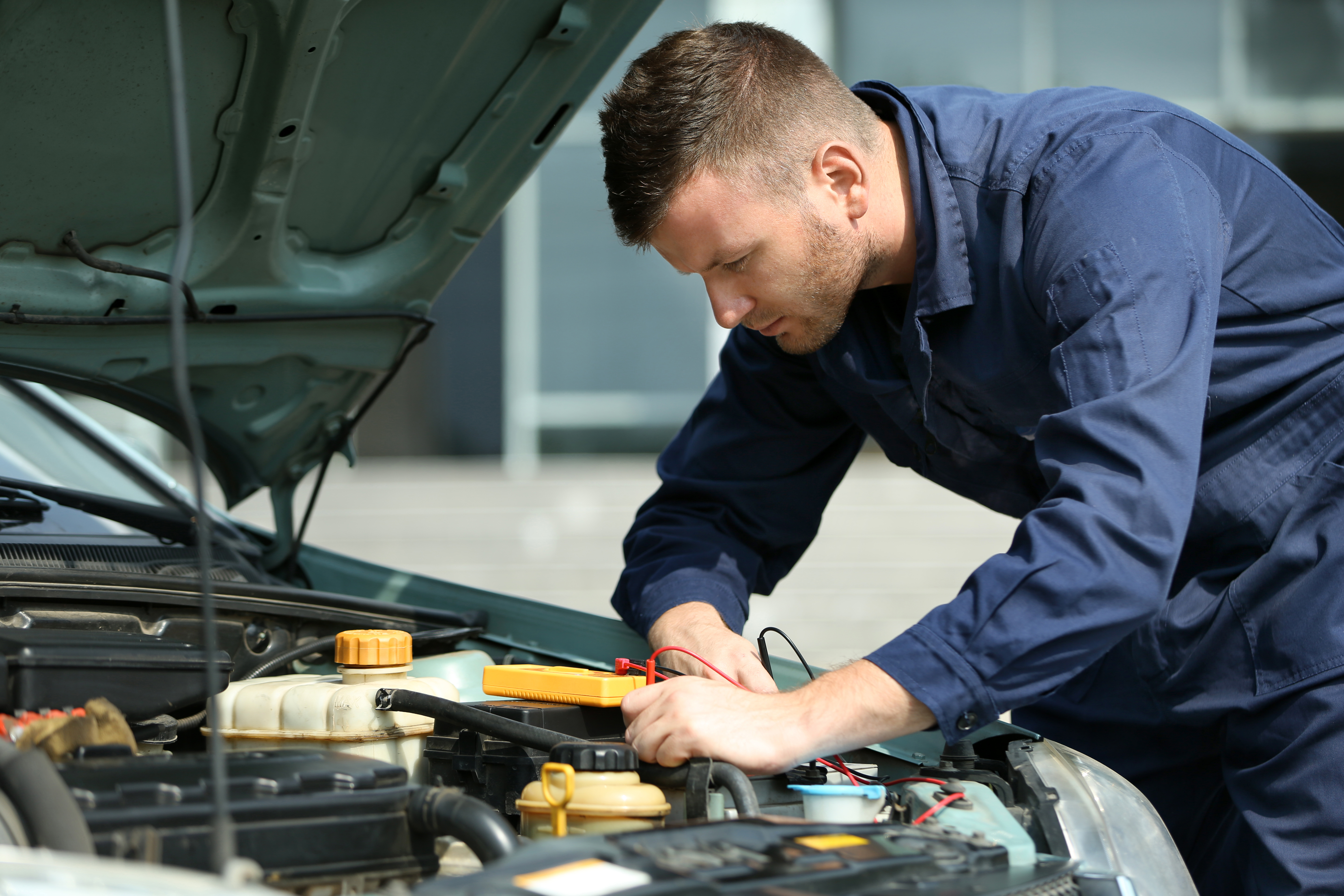 Mechanic with scan tool diagnosing car in open hood. | Source: Shutterstock