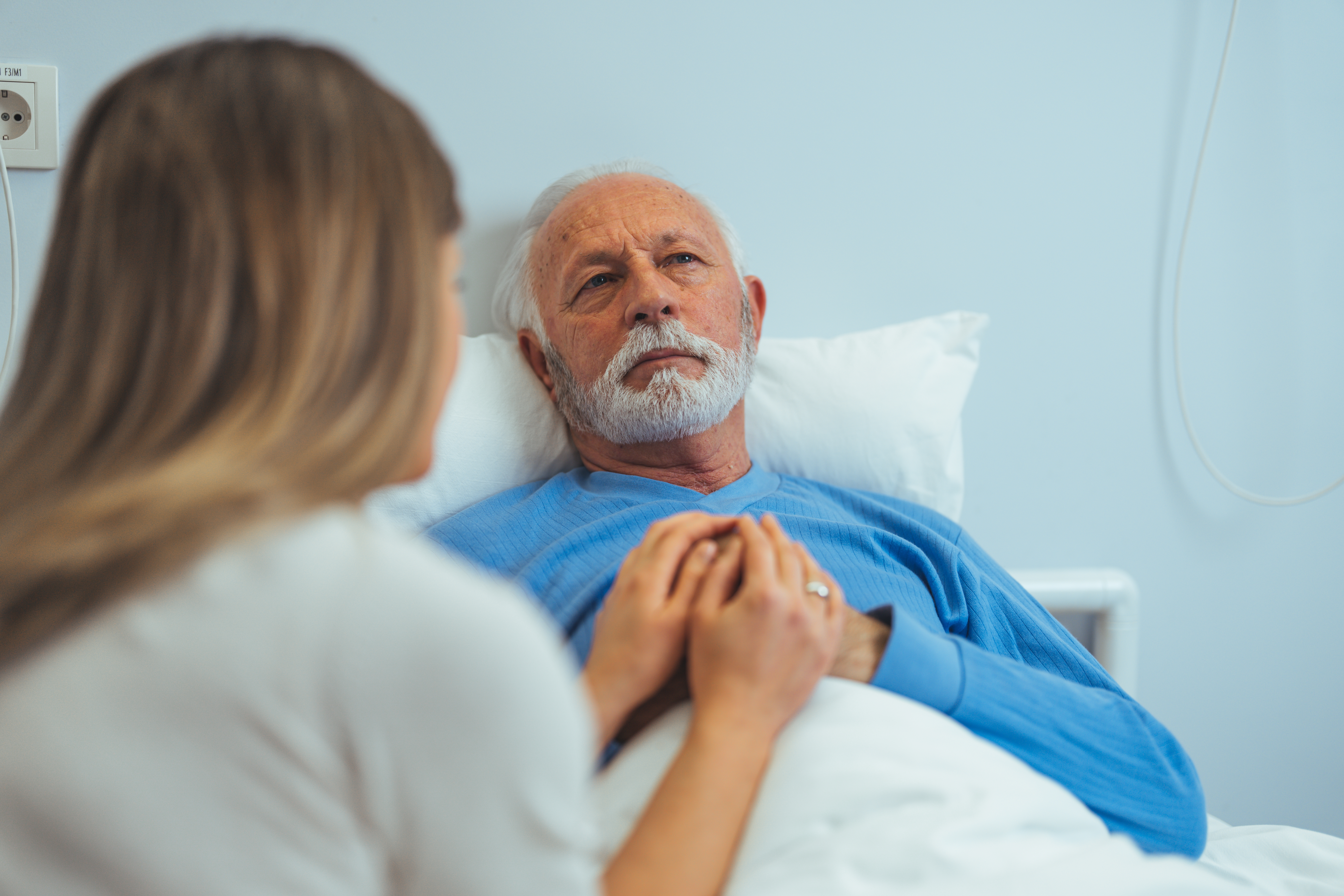 A woman visiting an older man in a hospital room | Source: Shutterstock
