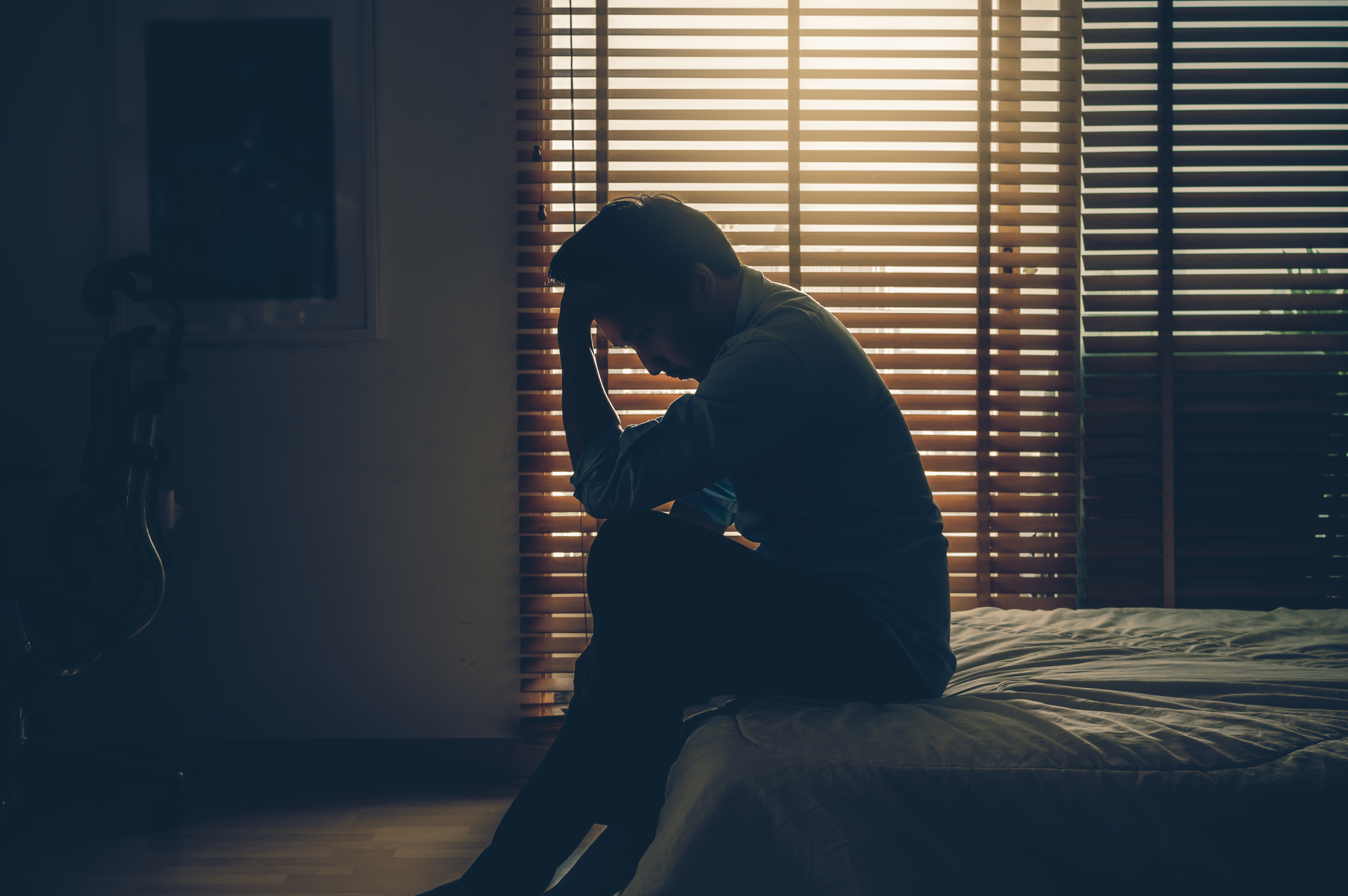 Sad businessman sitting head in hands on the bed in the dark bedroom with low light environment. | Source: Shutterstock