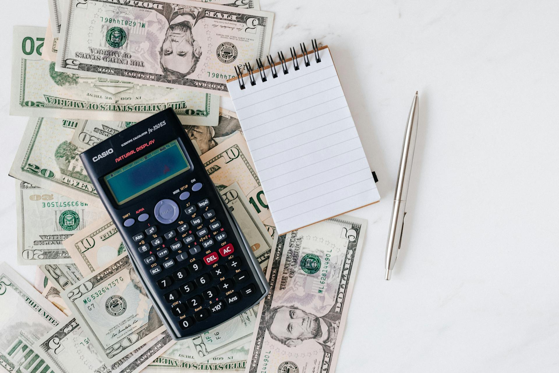 Calculator and notepad on dollar bills | Source: Pexels