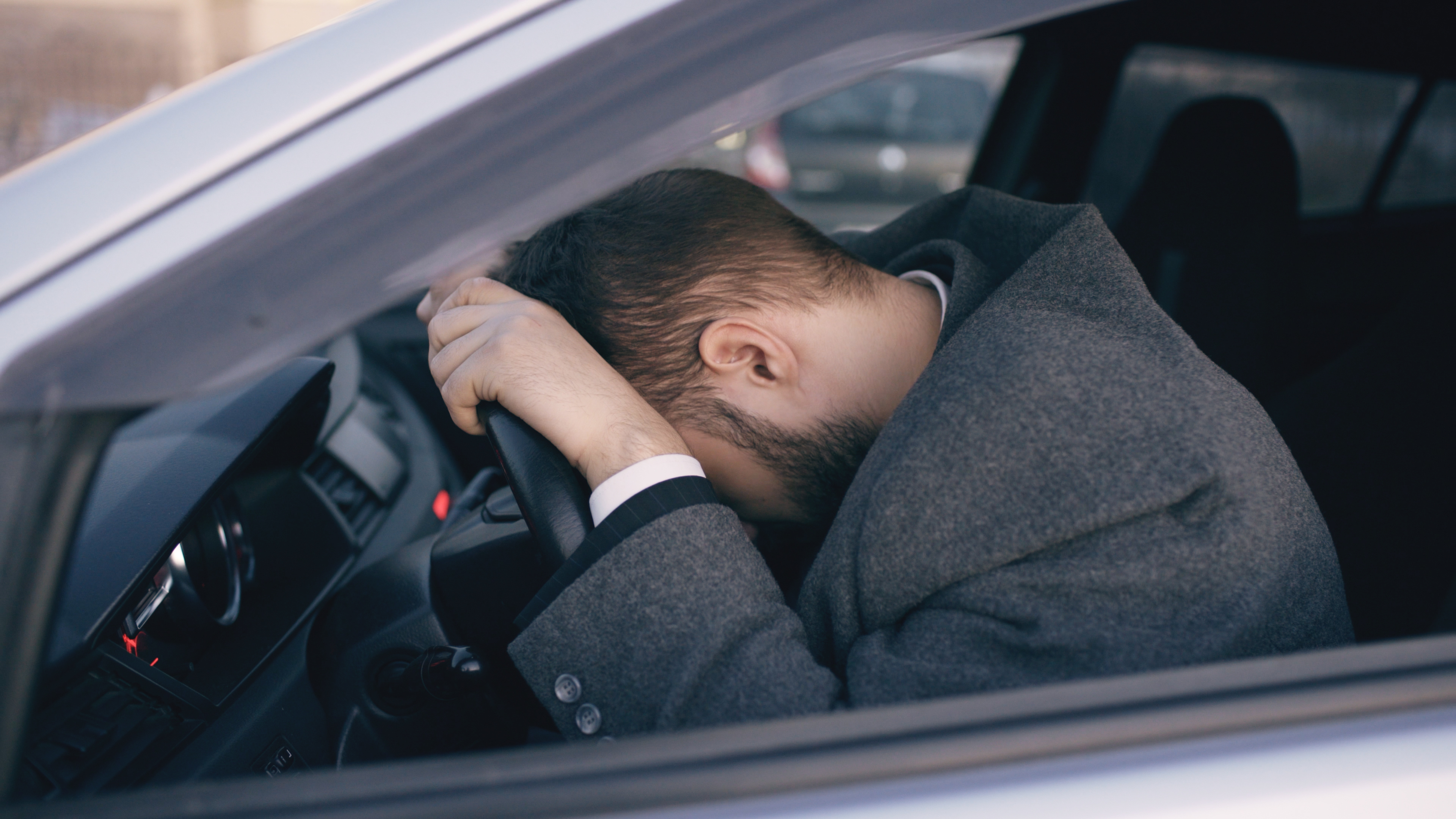 Bearded man sitting in car very upset and stressed after hard failure and moving in traffic jam. | Source: Shutterstock