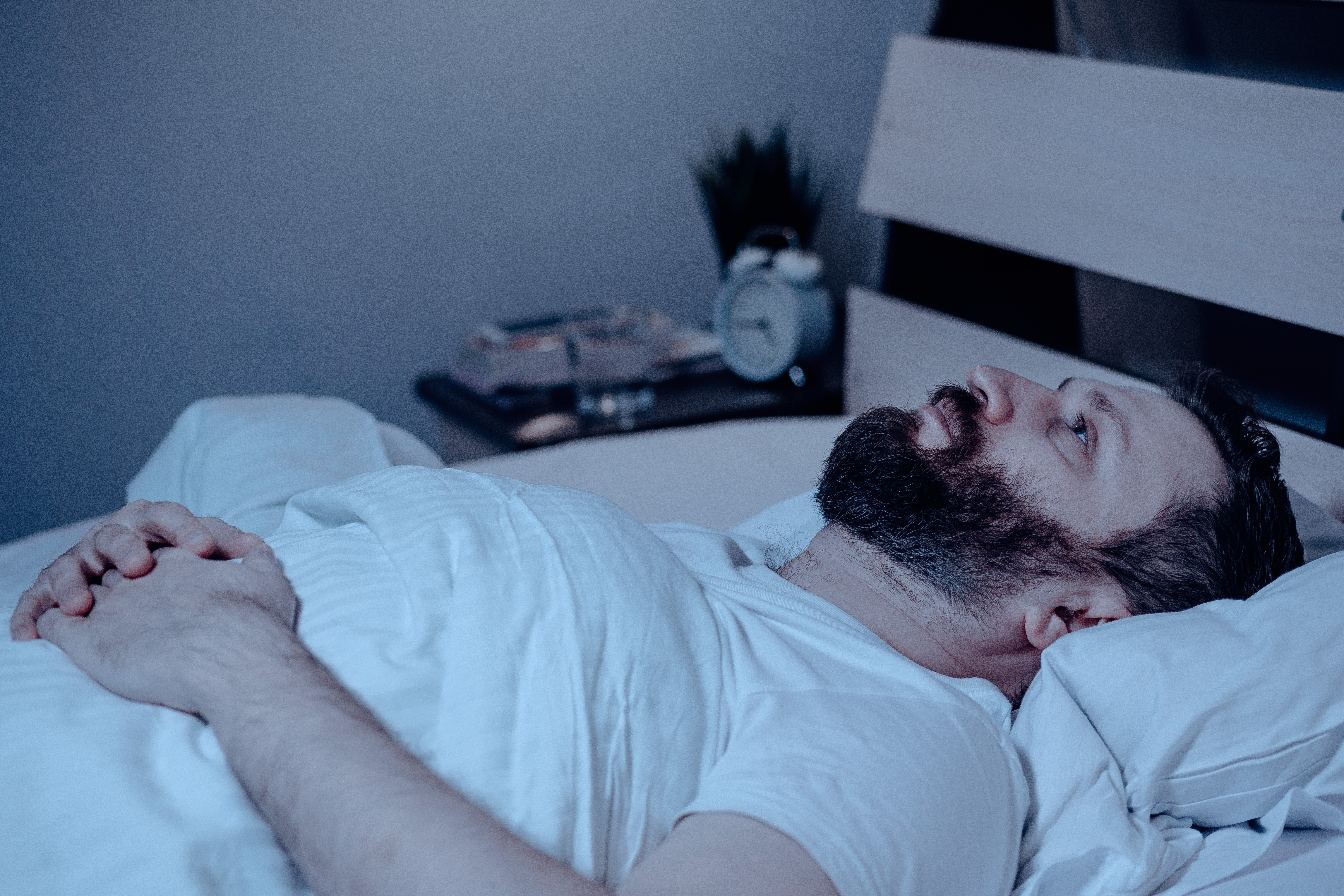A bearded man in bed at night cannot sleep, is unhappy and very tired. | Source: Shutterstock