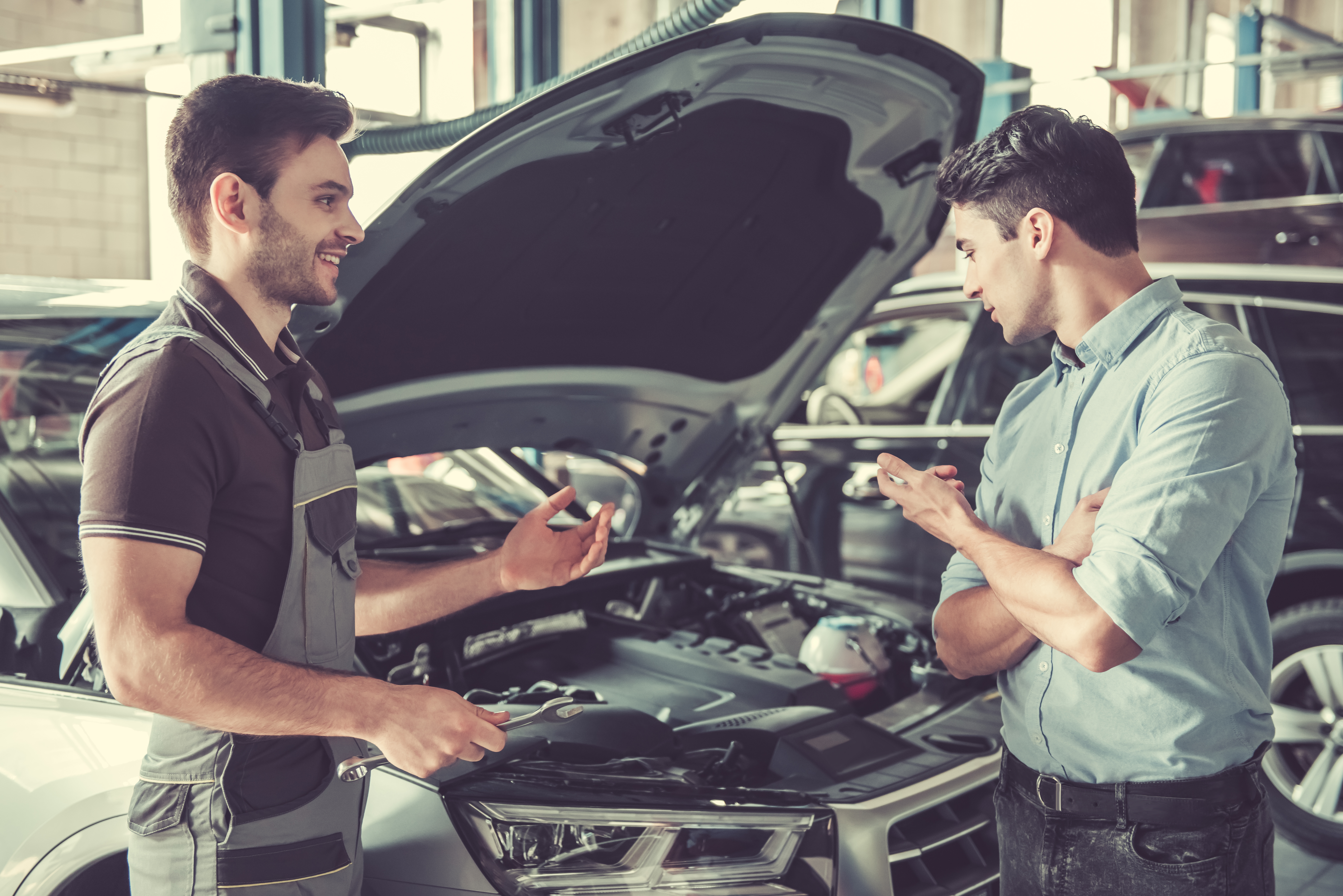 At the auto service. Handsome young auto mechanic in uniform is talking with a client and smiling. | Source: Shutterstock